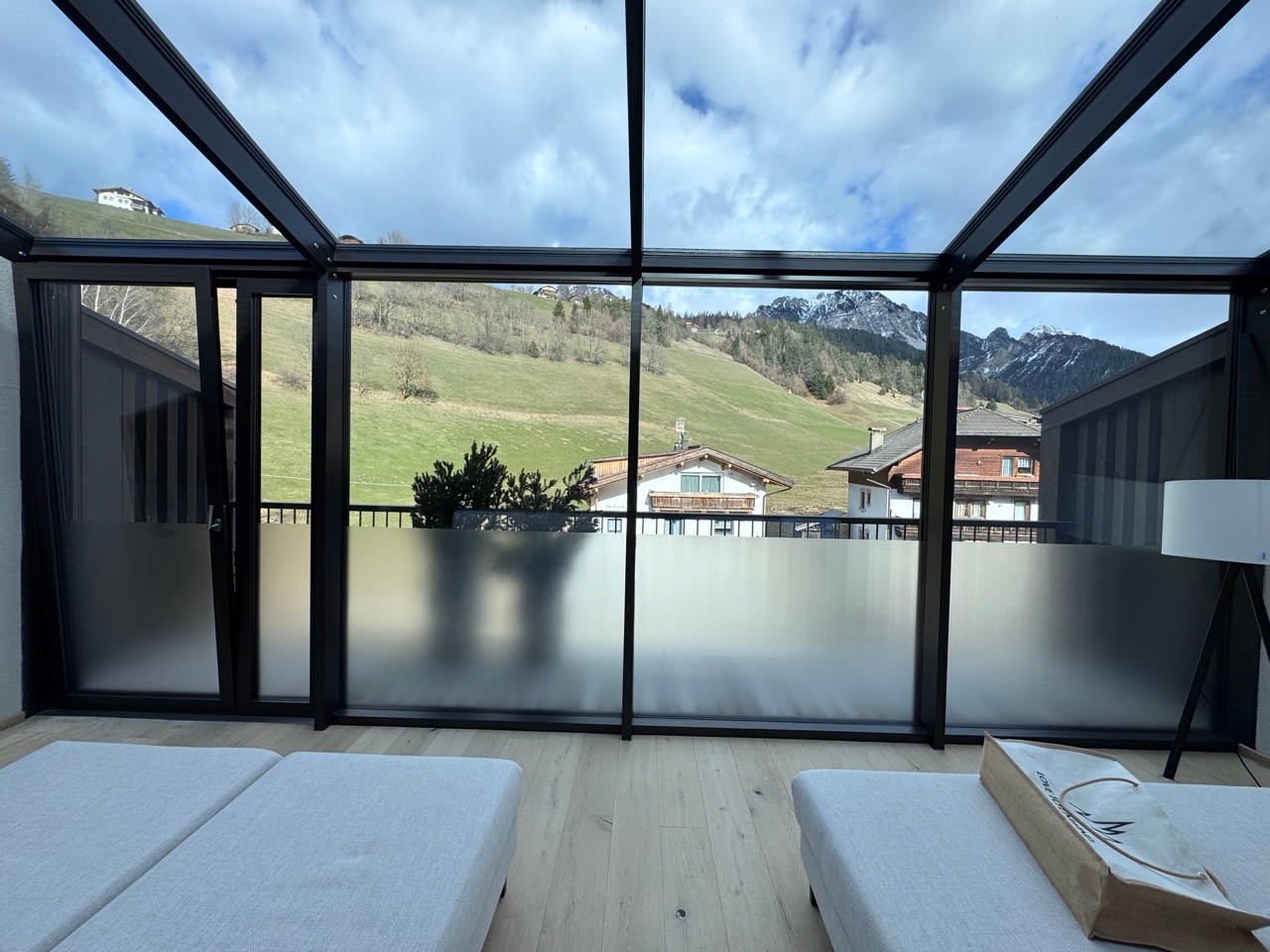 Panoramic lounge at AMA Stay with glass roof and views of green hills and Dolomites peaks