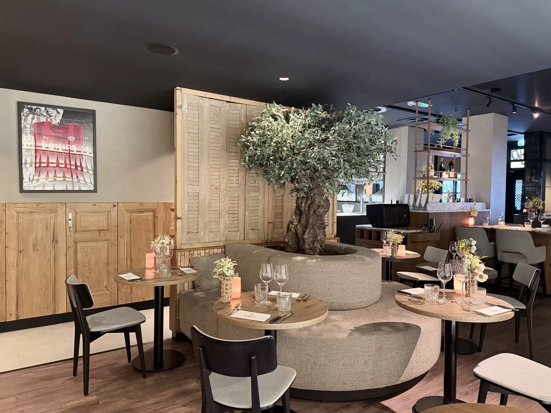 Manca Veldhoven dining room with olive tree, round seating, bar, and tables